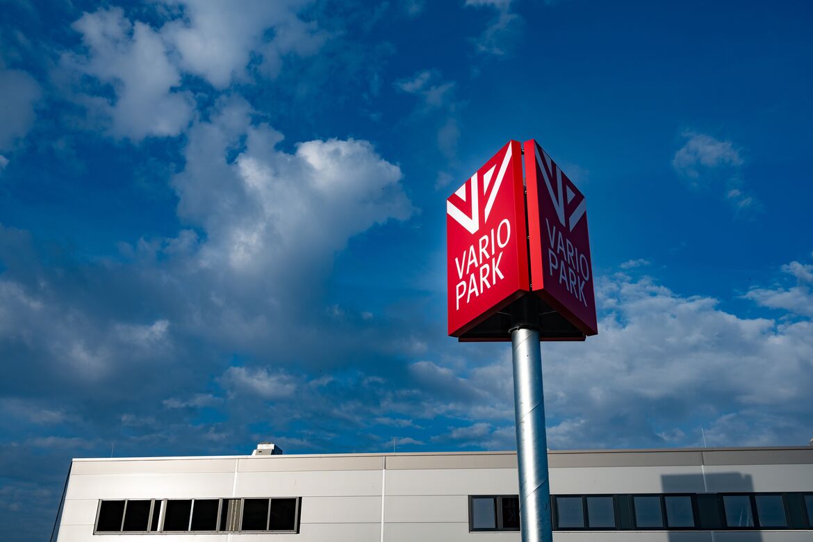 Werbepylon mit dem Logg der VarioPark vor blauem Himmel und einer Teilansicht des Gebäudes