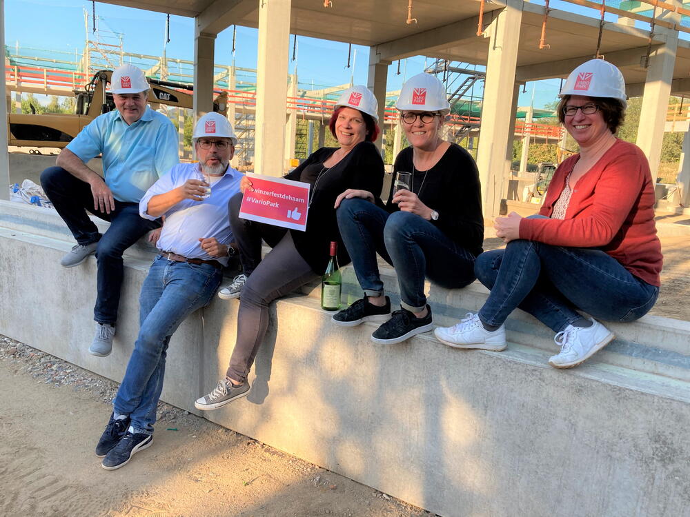 Das 5köpfige VarioPark-Team mit Helmen und Weingläsern auf der Baustelle