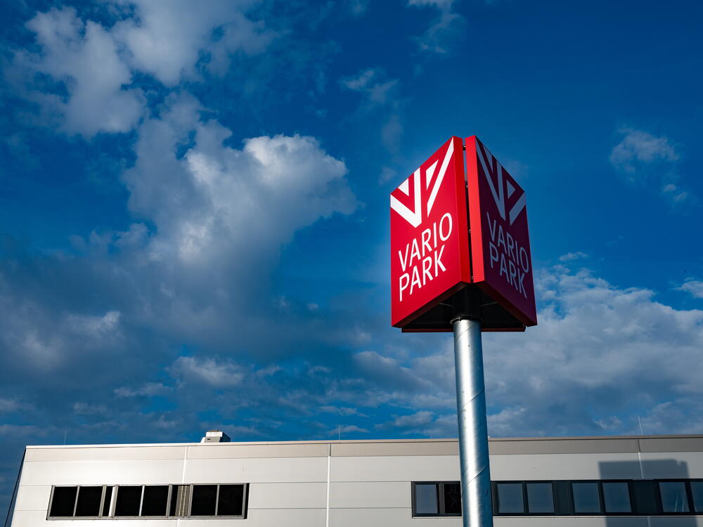 Werbepylon mit dem Logg der VarioPark vor blauem Himmel und einer Teilansicht des Gebäudes